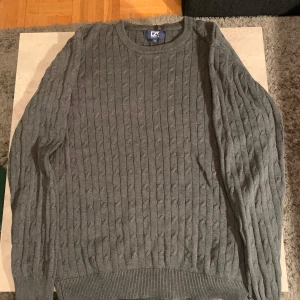 Grå fin stickad tröja från Cutter & Buck och storleken är S, färgen är mörk grå, kom ed frågor med mera - Säljer en snygg grå stickad tröja från Cutter & Buck i storlek S. Färgen är mörk grå,Tröjan har ett klassiskt kabelstickat mönster och långa ärmar. Perfekt för höst och vinter, den är både stilren och bekväm. Passar bra till både vardag och lite finare tillfällen, kom med frågor med mera
