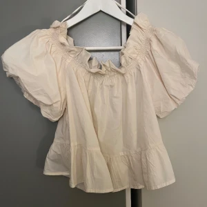 Beige offshoulder topp från Gina Tricot - Säljer en superfin beige offshoulder topp från Gina Tricot. Den har puffiga korta ärmar och en volangdetalj vid halsen. På bild 3 ser man toppen på fast i en annan färg. Använd 1 gång