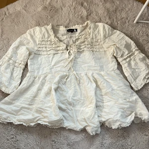 Blus - En vit blus med många volanger.Den ser på bilderna ut att vara lite gul men så är inte fallet.