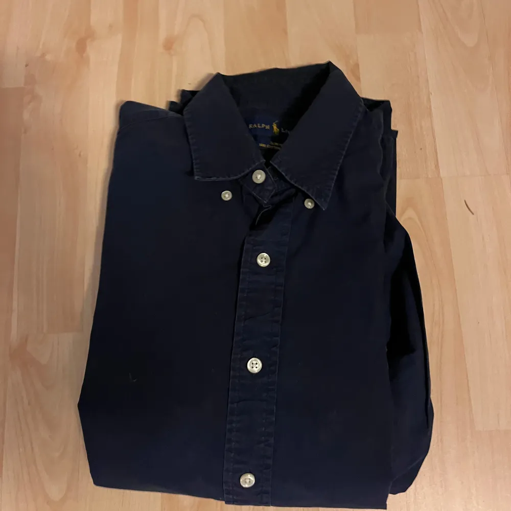 Snygg svart skjorta från Ralph Lauren i mycket bra skick. Den har långa ärmar och klassiska knappar framtill. Perfekt för både vardag och festliga tillfällen. Skjortan är i storlek herr M och har en stilren design med en liten broderad logga på bröstet.. Skjortor.