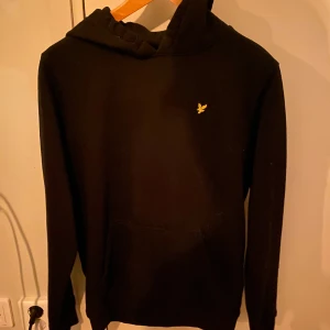 Svart hoodie med logga - Säljer en stilren svart hoodie med en liten gul logga på bröstet. Den är i bra skick och perfekt för både höst och vinter. Tröjan har en klassisk passform med långa ärmar och en bekväm huva. Perfekt för en avslappnad look eller för att hålla sig varm under kyliga dagar. Pris kan diskuteras 