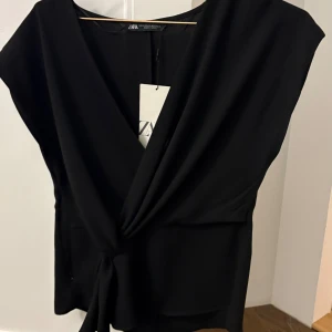 Svart omlottopp från Zara - Snygg populär svart omlottopp från Zara med knytning framtill. Toppen passar för alla tillfällen och är andvänd. Säljer för att jag känner att den inte riktigt passar mig💕