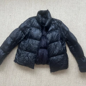 Marinblå dunjacka från Uniqlo - Säljer en svart ultralätt dunjacka från Uniqlo. Jackan har en quiltad design med dragkedja framtill och långa ärmar. Perfekt för kyliga dagar när du vill hålla dig varm utan att känna dig tung.