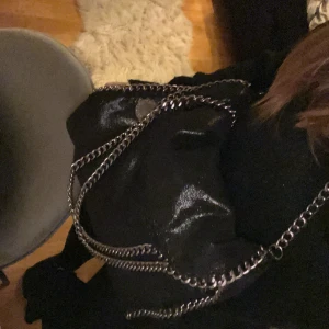 Svart axelväska från Stella McCartney - Snygg svart axelväska från Stella McCartney med kedjedetaljer längs kanterna och axelremmen. Väskan har en rund metallbricka med logotyp. Perfekt för en stilren look. Obs! Vet ej om väskan är äkta då jag köpte den secondhand 💕