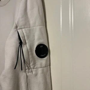 C.P. Company - Säljer en stilren vit sweatshirt från C.P. Company. Storlek L men passar M ser smutsigt ut på bild men den är i fint skick 