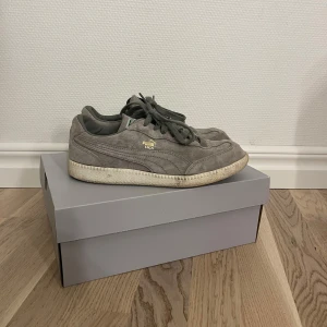 Grå sneakers från Puma - Snygga grå sneakers från Puma med klassisk design och snörning. Skorna har täcken på användning och är något smutsiga som säkert går att få bort🩶