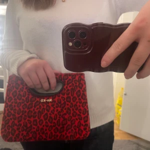 Röd leopardmönstrad väska från NA-KD - Snygg röd leopardmönstrad väska från NA-KD med praktiskt handtag. Perfekt för att ge en färgklick till din outfit. Aldrig använt den därav säljer jag den. Pris kan diskuteras 