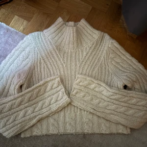 Beige stickad tröja från & Other Stories - Mysig beige stickad tröja från & Other Stories i storlek XS. Perfekt för kyliga dagar med sitt flätstickade mönster och höga krage. Tröjan har långa ärmar och är superbekväm. Använt endast en gång så ser ut som ny, köpte den för 800 kr så materialet är väldigt hållbart❤️