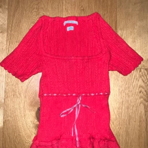 Röd ribbad topp med knytband - Säljer en superfin röd ribbad topp med kortärmad design. Den har ett sött knytband i midjan och volangdetaljer längst ner. 
