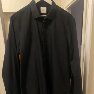 Svart skjorta från Next - Snygg svart skjorta från Next Tailoring i storlek L. Skjortan har en klassisk krage och knappar framtill. Perfekt för en stilren look.
