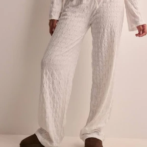 Vita mjukisbyxor med broderi från Nelly  - Mysiga vita mjukisbyxor med ett diskret broderat mönster. Byxorna har en loose passform och dragsko i midjan för extra komfort. Perfekta för en avslappnad dag hemma. Oanvända!