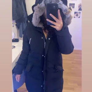 Svart vinterjacka från Hollies - Säljer en snygg svart parkajacka från Hollies i storlek 40. Jackan har en mysig pälsfodrad huva och praktiska dragkedjor. Använd förra vintern🤍