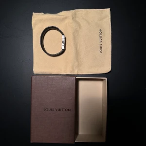 Louis Vuitton Armband - Säljer ett elegant svart armband från Louis Vuitton i mycket bra skick. Armbandet har en stilren design med en metallplatta där Louis Vuitton-loggan är ingraverad. Det kommer med originalförpackning och en skyddande tygpåse. Perfekt för att ge en lyxig touch till din outfit! Armbandet är reversible och går därför att byta sida på det ifall man vill ha svart eller Louis Vuitton mönstret. Kostar ca 4500kr nytt. Mitt pris 1499kr. Storlek 19 cm
