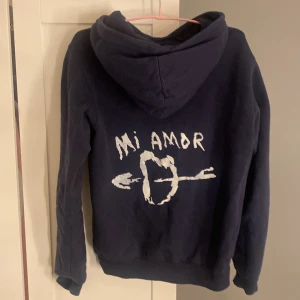 Mörkblå hoodie med tryck - Säljer en mörkblå hoodie med trycket 'Mi Amor' på ryggen, fickan där fram är däremot bortsprättad men inget som syns. Köpt här på Plick, hör av dig om du är intresserad! 