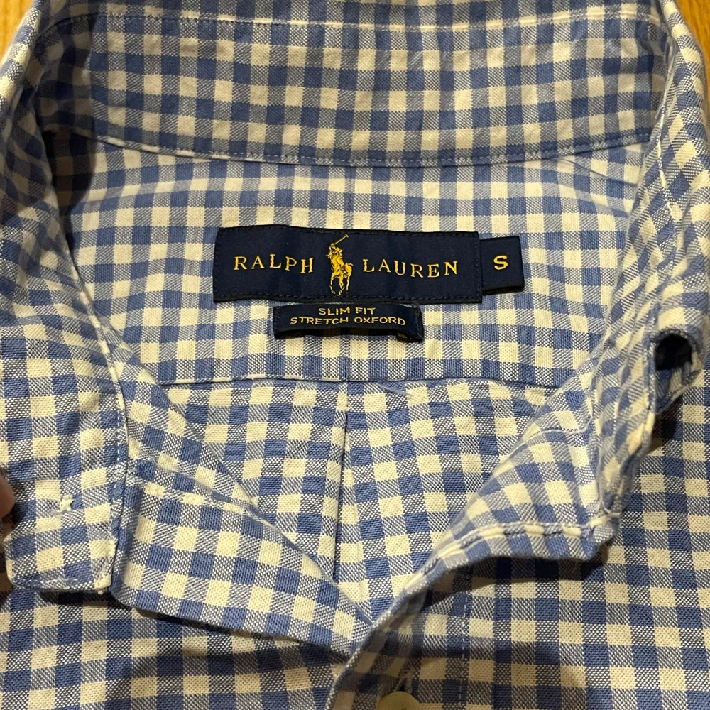 Säljer en snygg blå och vit rutig skjorta från Ralph Lauren i storlek S. Skjortan är i slim fit och tillverkad av stretchig bomull, vilket gör den både bekväm och stilren. Den har långa ärmar och knappar framtill. Perfekt för både vardag och fest! 🕺 pris:199kr🌟. Skjortor.