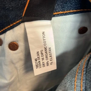 Mörkblå jeans från Nudie Jeans - Säljer ett par snygga mörkblå jeans från Nudie Jeans i modellen Lean Dean. De är tillverkade av 99% ekologisk bomull och 1% elastan för en bekväm passform. Perfekta för både vardag och fest! 🕺
