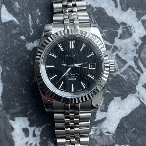  Seiko Mod- black datejust - Hej! Jag säljer nu en helt ny automatisk Seiko Mod med en elegant vågmönstrad svart urtavla. Inspirerad av de klassiska datejust modellerna. Priset av klockan kan diskuteras vid smidig affär!   Hör gärna av dig om du har frågor eller funderingar!