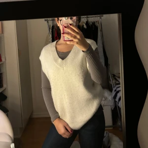 Vit stickad väst - Säljer en superfin vit stickad väst i normal passform. Perfekt för lager-på-lager under höst och vinter. Den har en v-ringad design som gör den både stilren och bekväm. Passar perfekt över en långärmad tröja för en mysig look.