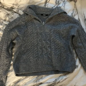 Grå stickad tröja från Bikbok - Mysig grå stickad tröja från Bikbok med dragkedja vid halsen. Perfekt för kyliga dagar med sitt kabelstickade mönster och ribbade kanter. Passar både till vardags och lite finare tillfällen. 🧶