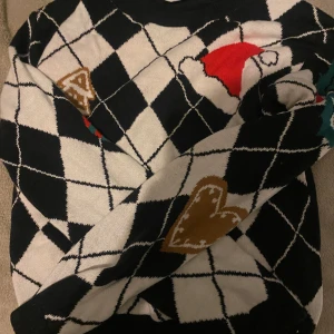 En jultröja från H&M - Säljer en jultröja från H&M med rutigt mönster och hjärtan. Tröjan har långa ärmar och är perfekt för kyligare dagar. Den har en mysig med inslag av rött och brunt.