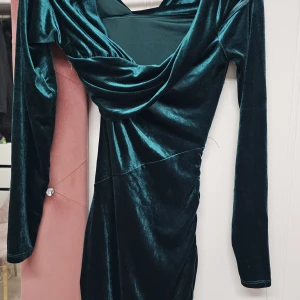 Mörkgrön sammetsklänning använd en gång pris kan diskuteras - Elegant mörkgrön klänning i mjukt sammetstyg med draperad framsida. Klänningen har långa ärmar och en smickrande passform som framhäver figuren. Perfekt för en stilfull kväll.