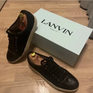 Svarta sneakers från Lanvin - Snygga svarta sneakers från Lanvin med klassisk design och snörning. Skorna har en vit sula och är perfekta för en stilren look. Levereras med originalkartong.OBS hål i sulan, bild tre och fyra.