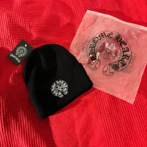 Säljer en snygg svart mössa från Chrome Hearts i nytt skick. Den är stickad och har en broderad logga framtill. Perfekt för att hålla sig varm och stilren under de kallare månaderna. Kommer med originalförpackning och etikett. Passar perfekt till både vardag och fest! Helt Ny. S/M