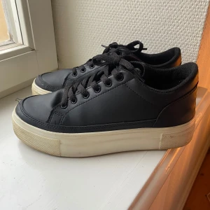Svarta sneakers från NLY Shoes - Säljer ett par svarta sneakers från NLY Shoes i bra skick. De har en klassisk design med snörning och en vit sula som ger en snygg kontrast. Perfekta för vardagsbruk och passar till det mesta i garderoben. Skostorlek EU 37.