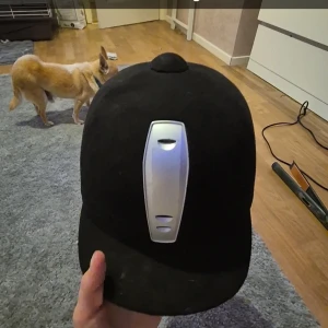 Svart ridhjälm med silverdetalj - Säljer en stilren svart ridhjälm med en silverfärgad ventilationsdetalj framtill. Hjälmen har en klassisk design och är perfekt för ridning.