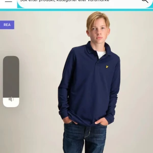 Mörkblå pikétröja från Lyle & Scott - Säljer en snygg mörkblå pikétröja från Lyle & Scott. Den har långa ärmar och en klassisk krage med knappar. Perfekt för både vardag och lite finare tillfällen. Den ikoniska loggan i gult pryder bröstet. Passar perfekt till jeans eller chinos!