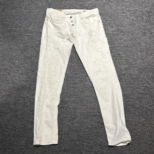 Vita jeansbyxor från dondup  - Säljer ett par vita jeansbyxor från dondup med en unik distressed look. De är vita slitningar över hela jeansen som ni kan se på bild 2. Byxorna har en knappgylf och klassisk femficksdesign. Perfekta för en trendig och avslappnad stil.