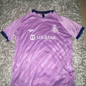 Al nassr tröja - Säljer en snygg lila fotbollströja med Ronaldo 7 på ryggen. Tröjan har korta ärmar och ett coolt mönster framtill. Perfekt för fotbollsfans som vill ha något unikt i garderoben.