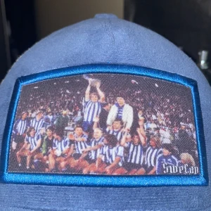 Blå keps med fototryck - Säljer en blå keps med ett coolt fototryck på framsidan. Kepsen har en vit mesh-baksida för bra ventilation och en justerbar rem för perfekt passform. Perfekt för sommarens alla äventyr eller bara för att ge din outfit en sportig touch!