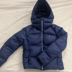 Blå dunjacka från Polo Ralph Lauren - Säljer denna jätte snygga och populära vinter jackan från Ralph lauren.😍 Storlek XL i barn/ 16 år men jag tycker att den är liten i storleken. Aldrig använd och har taggen kvar. Inte några defekter eller liknande heller. Mörkblå med Ralph lauren loggan i rosa.💕                                           Skriv gärna till mig vid frågor eller liknande💞