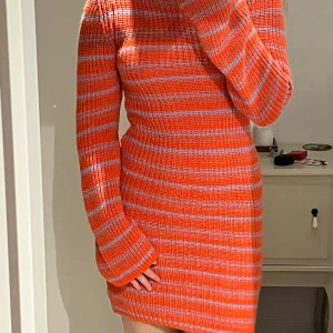Orange och lila randig stickad klänning - Superfin stickad klänning i orange och lila med randigt mönster. Den är tight och har långa armar. Klänningen är kort och ger en snygg siluett🤩🎉