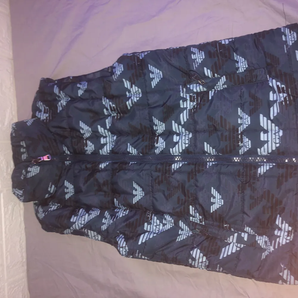Säljer en snygg pufferjacka från Armani Jeans i storlek S. Jackan har ett coolt mönster i svart och blått med dragkedja framtill. Perfekt för höst och vinter när du vill hålla dig varm och stilren. Passar både till vardags och lite mer uppklädda tillfällen. 🖤💙. Takit.