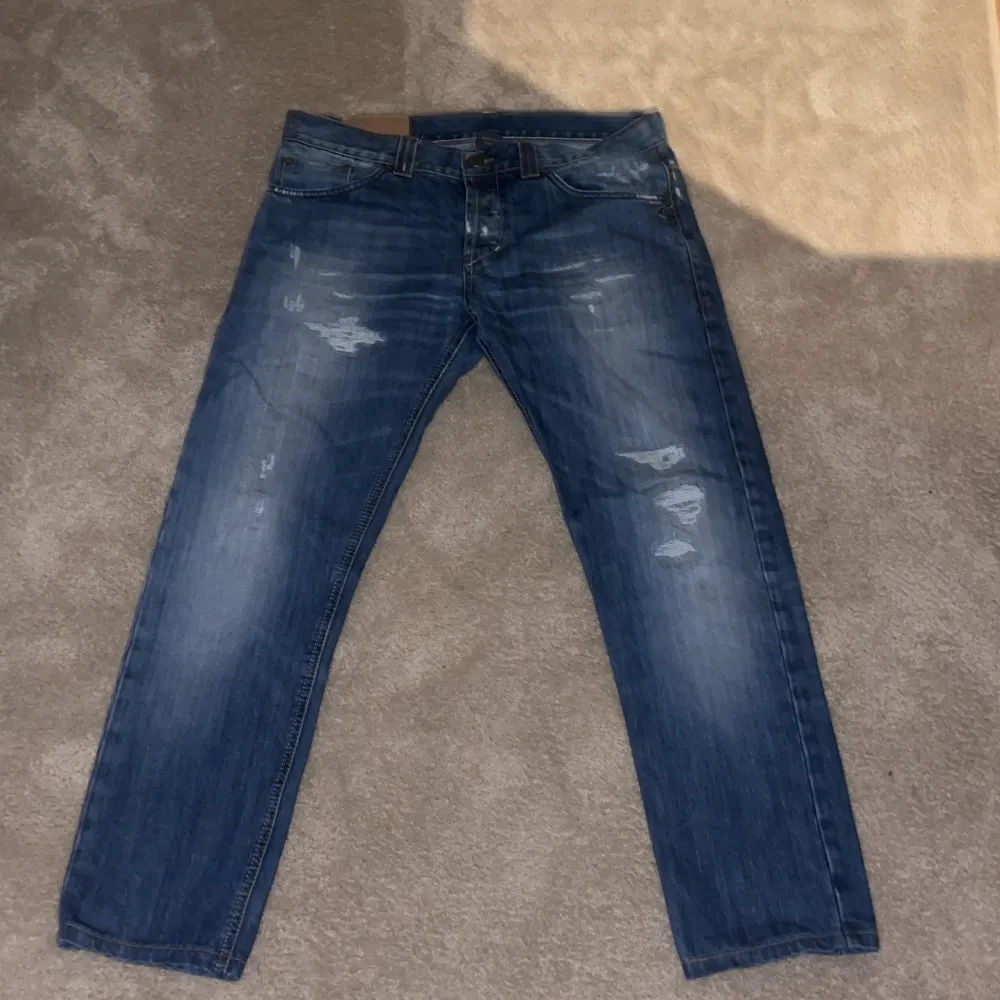 Säljer ett par snygga blå jeans från Dondup med coola slitningar. De har en klassisk femficksdesign och en bekväm passform. Perfekta för en avslappnad stil och funkar året runt. Passar både till vardags och fest!. Jeans & Byxor.