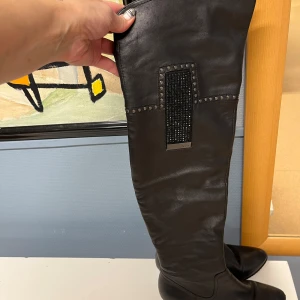 Svarta stövlar med pälsfoder - Snygga svarta stövlar i skinn med dragkedja och klack. De har en cool detalj med nitar och glittrande paljetter på sidan. Insidan är fodrad med ull foder, perfekt för kalla dagar. Sulan är robust och ger bra grepp. 