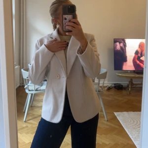 Vit kavaj - Säljer en stilren beige/rosa kavajen i mycket bra skick. Den har en klassisk design med en knapp framtill och långa ärmar. Perfekt för både vardag och festliga tillfällen. Passar bra till jeans eller klänning för en chic look. Kavajen är i ett tjockare material som gör att den passar perfekt som jacka. 