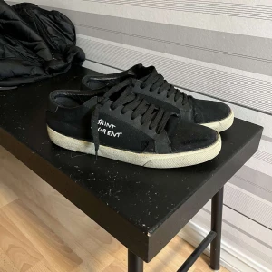 Svarta sneakers från Saint Laurent - Säljer ett par svarta sneakers från Saint Laurent i bra skick. De har en klassisk design med snörning och vit sula. Perfekta för både vardag och fest. Har inget og därav priset 