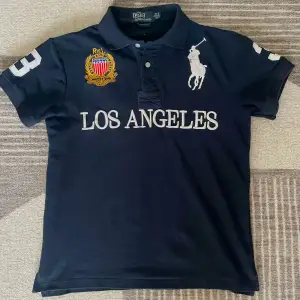 Säljer en snygg svart pikétröja från Ralph Lauren med 'Los Angeles' broderat på framsidan. Den är i bra skick och perfekt för både vardag och fest. Passar dig som gillar stilrena plagg med en sportig touch. Den perfekta Chief Keef Skjortan. Storlek S men Går också som M