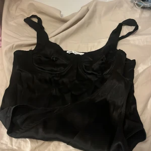 Svart klänning från Zara - Säljer en elegant svart klänning från Zara i storlek L. Klänningen är axelbandslös och har en mjuk, glansig finish som ger en lyxig känsla. .