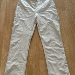 Krämfärgade PU-byxor från Gina Tricot - Säljer ett par snygga krämfärgade PU-byxor från Gina Tricot i storlek XL. Byxorna har en modern och stilren design med hög midja och raka ben. Perfekta för både vardag och fest! 🖤