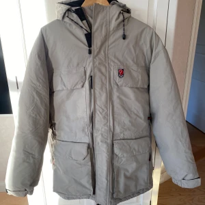 Beige vinterjacka från Fjällräven - Säljer en snygg och varm beige vinterjacka från Fjällräven Polar. Jackan har en praktisk huva och flera fickor framtill. Perfekt för kalla vinterdagar! 🧥❄️