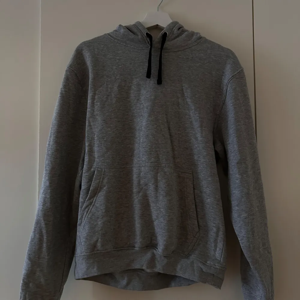 Säljer en grå hoodie i mjukt material med svarta snören i luvan. Perfekt för kyliga dagar och mysiga stunder. Den har en klassisk passform med en stor ficka framtill. Passar både till vardags och avslappnade tillfällen.. Tröjor & Koftor.