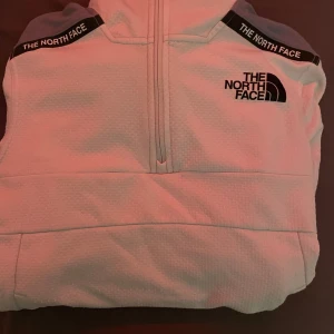 Vit hoodie från The North Face - Säljer en snygg vit hoodie från The North Face med grå detaljer på axlarna. Den har en halv dragkedja framtill och en stor logga på bröstet. Perfekt för kyliga dagar och passar till både vardag och träning. Superbekväm! Knappt använd och köpt 1200kr. Storlek Xs men passar även S. En liten fläck på armen men man tänker inte på den. Kan gå bort i tvätten (se sista bilden) 