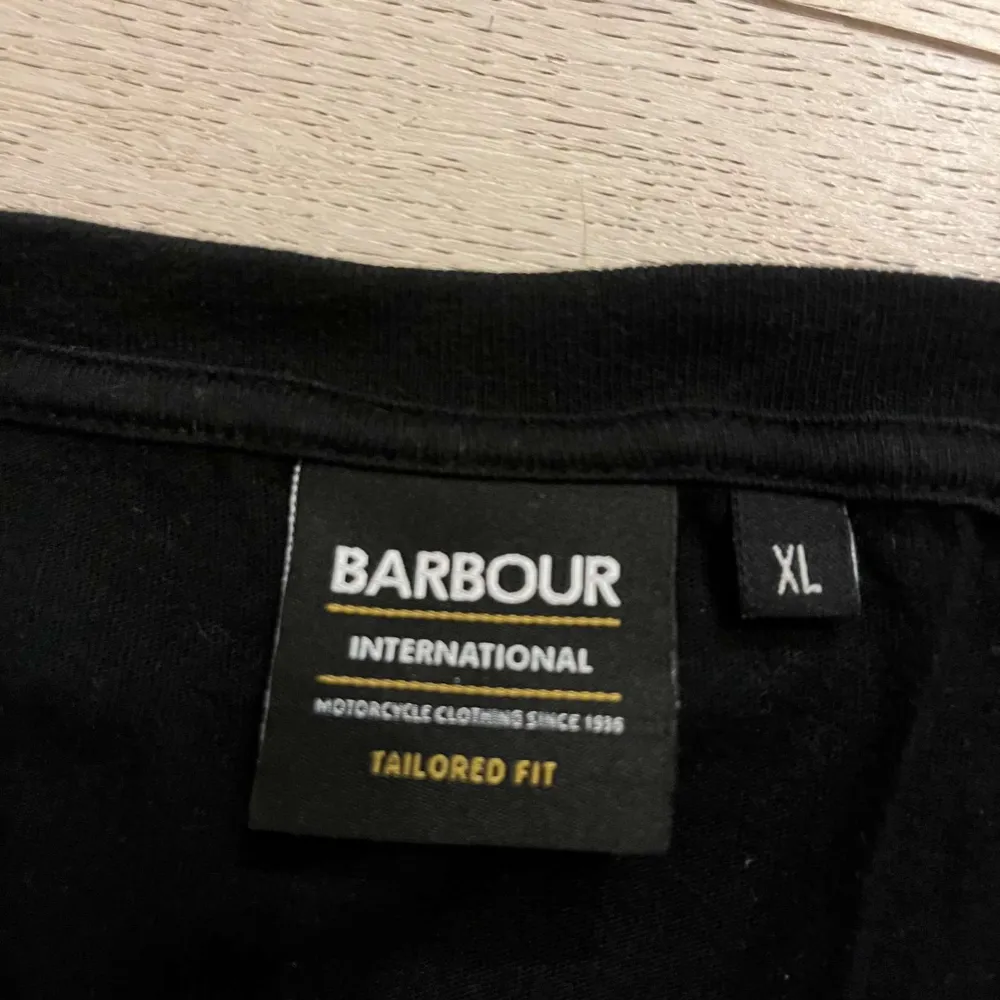 Säljer en svart t-shirt från Barbour International i storlek XL. Den har en klassisk design med korta ärmar och en gul logga på ärmen. Perfekt för en avslappnad stil eller som basplagg i garderoben.. Takit.