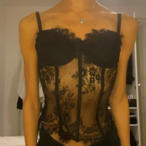 Svart spetskorsett - Säljer en elegant svart spetskorsett med blommigt mönster. Den har justerbara axelband och en genomskinlig design . Super bra skick !! Passar XS-M