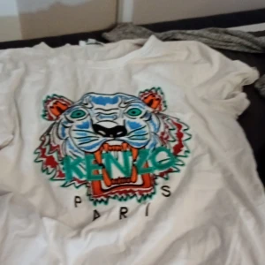Vit t-shirt med tigertryck från Kenzo - Säljer en cool vit t-shirt från Kenzo med ett färgglatt tigertryck på framsidan. T-shirten är kortärmad och perfekt för en avslappnad stil. Passar bra till både jeans och shorts. Perfekt för sommaren! 🐯