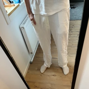 Vita byxor från Grunt - Säljer ett par vita bomulls/linne byxor från Grunt i storlek L/170. De är både bomull och linne, perfekt för en avslappnad stil. Byxorna har en loose passform och är idealiska för vår och sommar. Perfekta för en chill dag hemma eller en skön sommar dag. De är lite guld vid fötterna men det är inget som syns så mycket